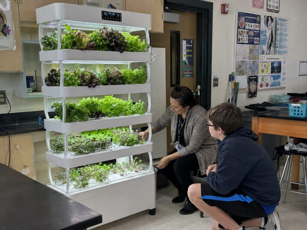 A teacher and student tending plants on a classroom Nutraponics grow shelf.